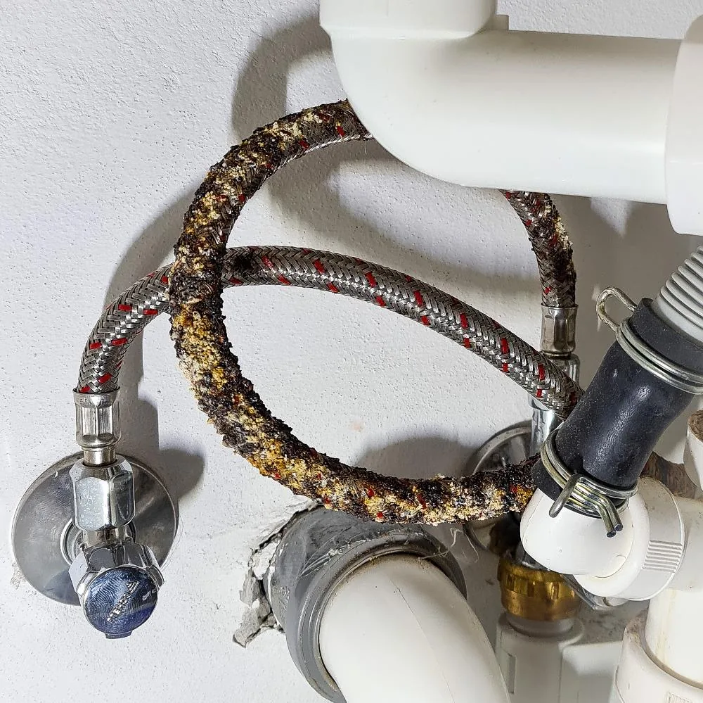 Eckventil mit zwei älteren Flexschläuchen unter einem Waschtisch